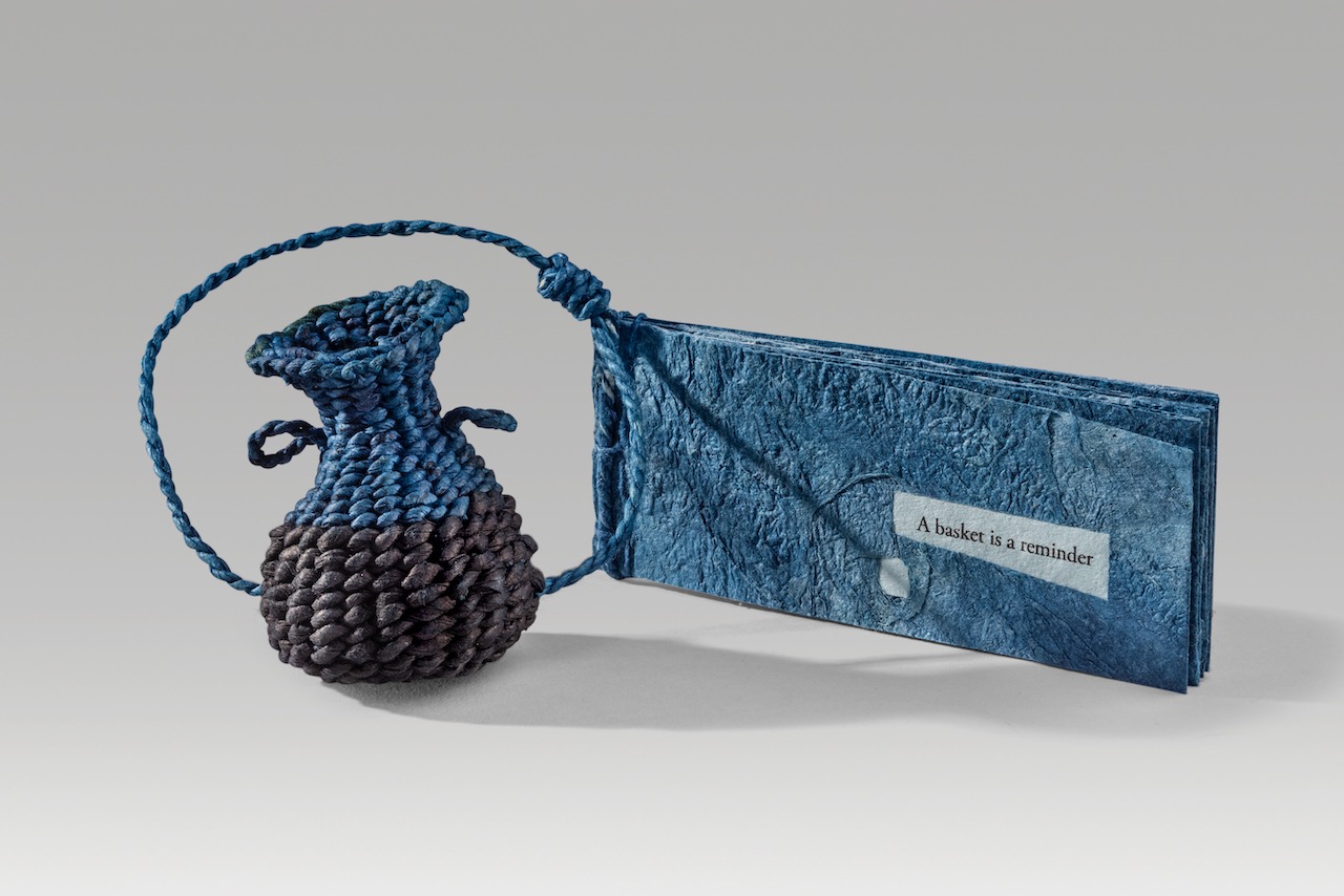A basket is a reminder (blue version) (2022). Indigo dye in paper thread and paper cord, on corded and twined hanji, combined with joomchi and inkjet print on hanji. Basket: 2.6 x 2 x 2.25”; book: 2 x 5 x 0.4” closed. One of a kind.